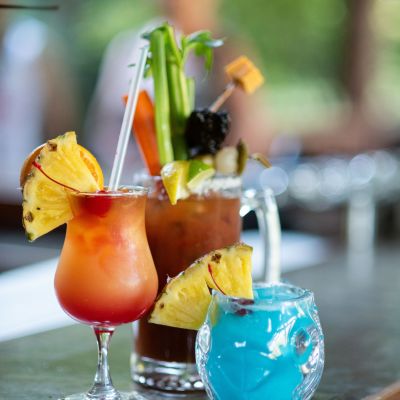 Three colorful cocktails with garnishes on a bar counter.