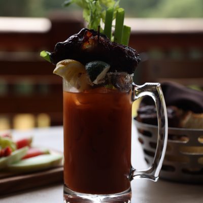 Bloody Mary with celery, lime, and bacon garnish on a patio table.